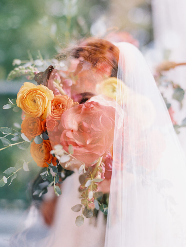 Double exposure of a bride’s serene profile with vibrant orange and pink blooms, creating an artistic and dreamy effect. Photographed on film by Lexie Vaccaro Photography.