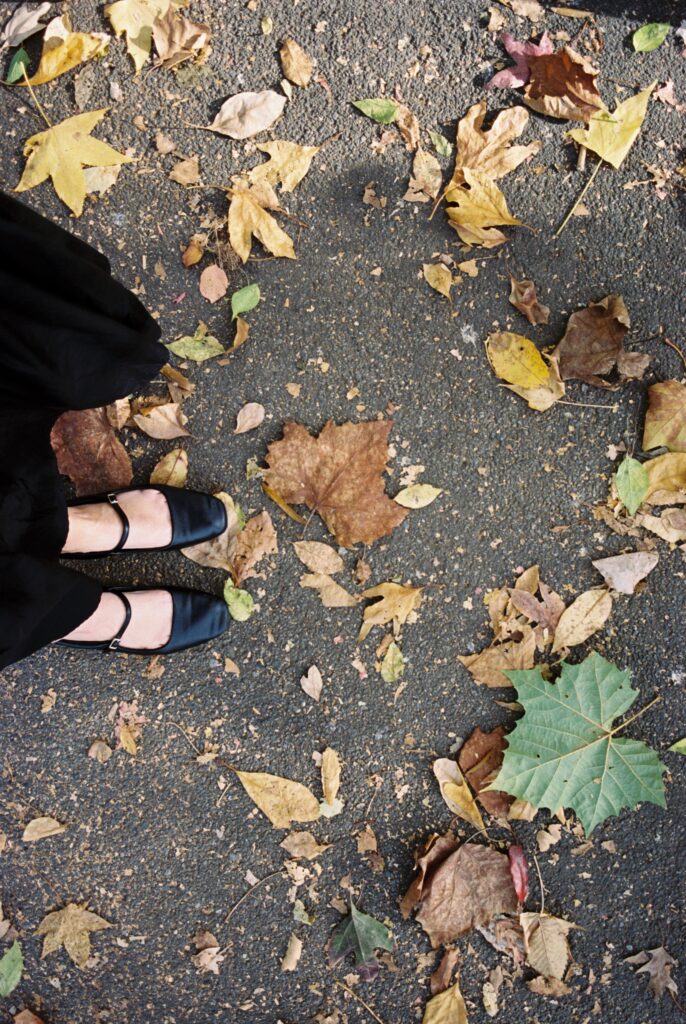 Film photo of autumn leaves scattered on a path in Central Park, with black satin  shoes in the frame, shot on Kodak Portra 400 film