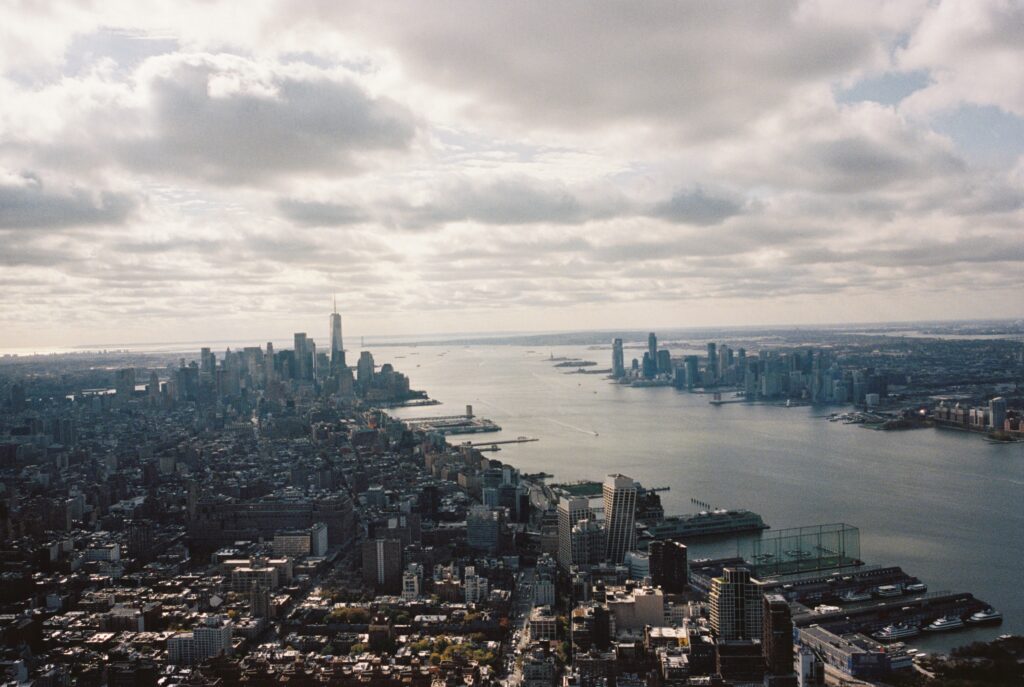 Aerial view of downtown Manhattan, the Hudson River, and Jersey City under a cloudy sky, captured on Kodak Portra 400 film using a Contax G1 camera.