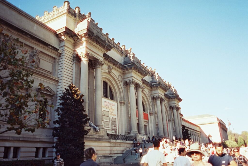 The Metropolitan Museum of Art in New York City, with sunlight highlighting its iconic columns and a bustling crowd on the steps. Captured on Cinestill film by Lexie Vaccaro Photography.