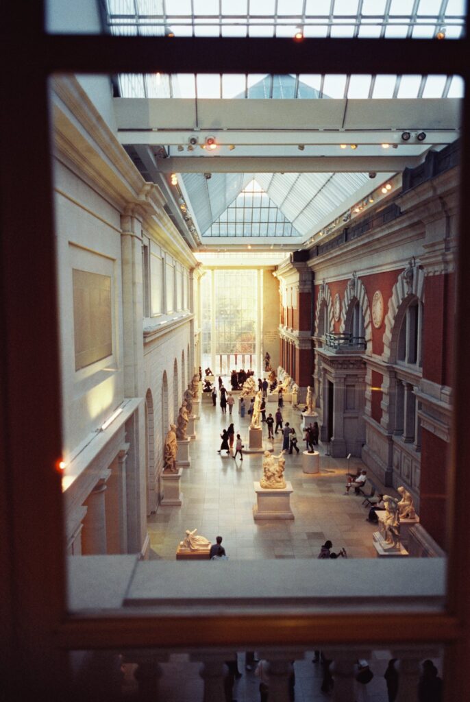 Film photo of the sunlit sculpture gallery at The Metropolitan Museum of Art in New York City, showcasing statues, visitors, and warm golden light, captured on CineStill film with a Contax G1 camera.