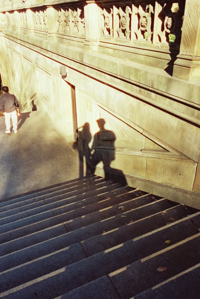 Film photo of shadows of a couple—my husband and I—cast on the stone wall near the stairs at Central Park, New York City, captured in golden light on CineStill film with a Contax G1 camera