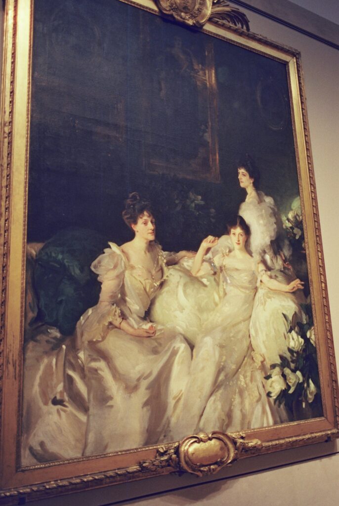 Film photo of an elegant portrait painting displayed at The Metropolitan Museum of Art, featuring three women in flowing gowns, captured on CineStill film with a Contax G1 camera.