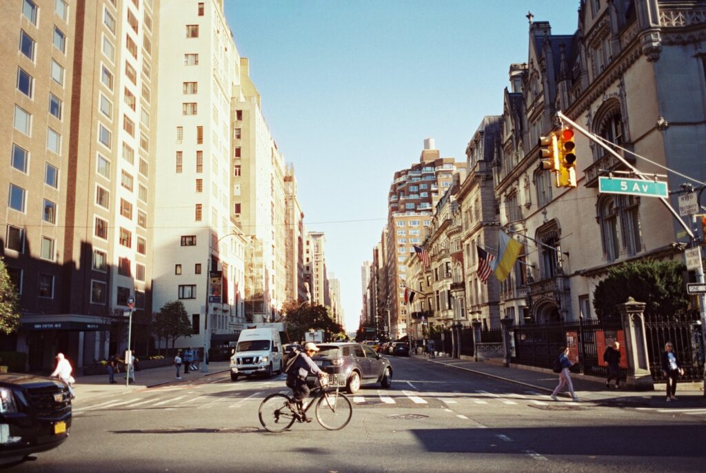 Film photo of a sunny street scene on Fifth Avenue in New York City, featuring cyclists, pedestrians, and iconic buildings, captured on CineStill film with a Contax G1 camera