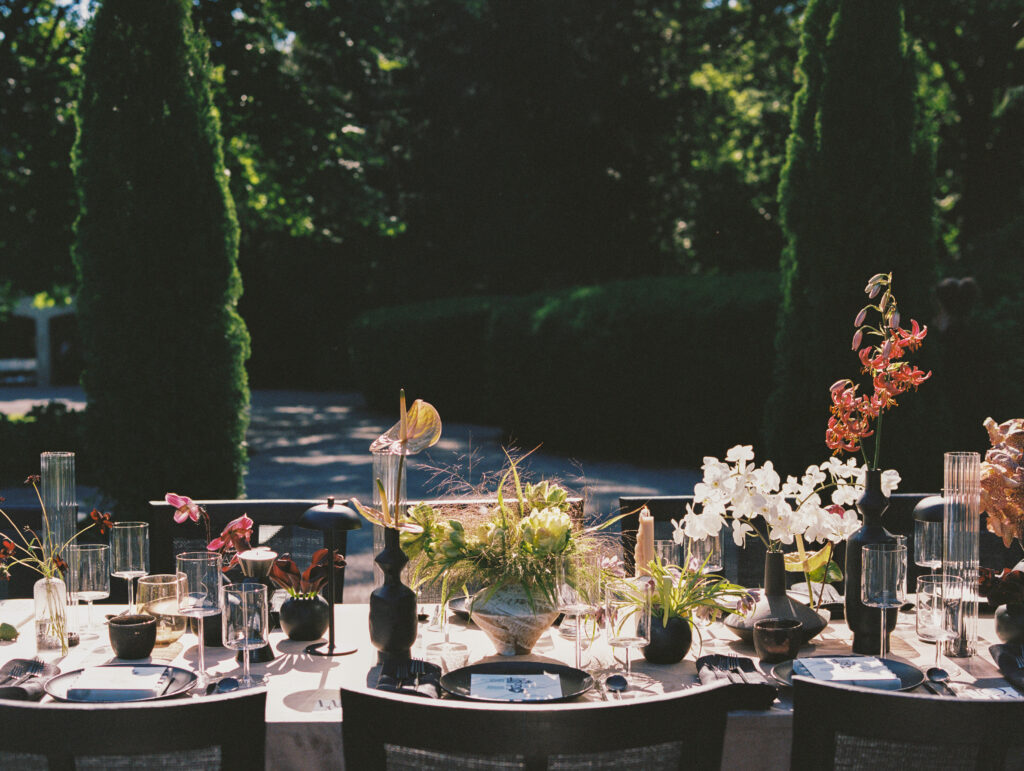 A modern, artful wedding tablescape at Greencrest Manor, adorned with sculptural floral arrangements, candlelight, and elegant tableware, captured on film in warm evening light.