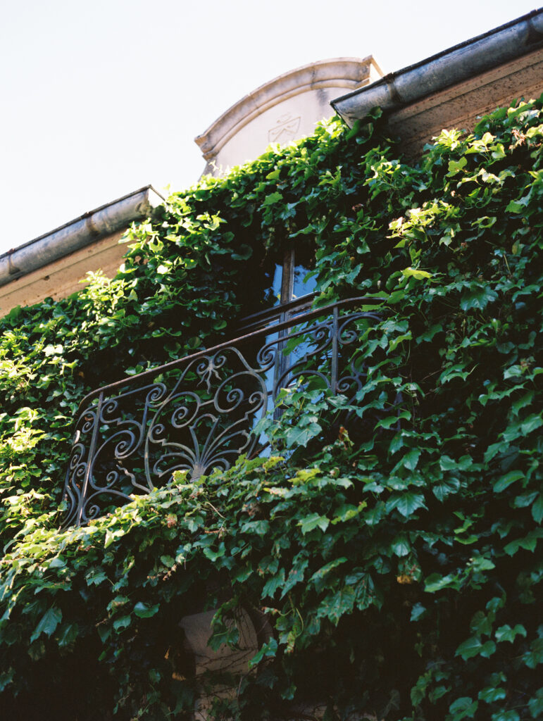 An ornate wrought-iron balcony draped in lush green ivy at Greencrest Manor, evoking a romantic European château ambiance.