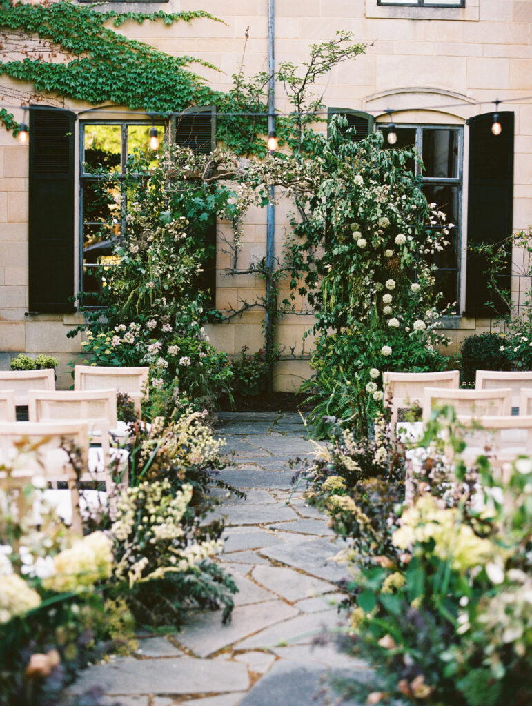 A romantic outdoor wedding ceremony setup at Greencrest Manor, featuring lush floral arrangements, stone pathways, and ivy-covered architecture.