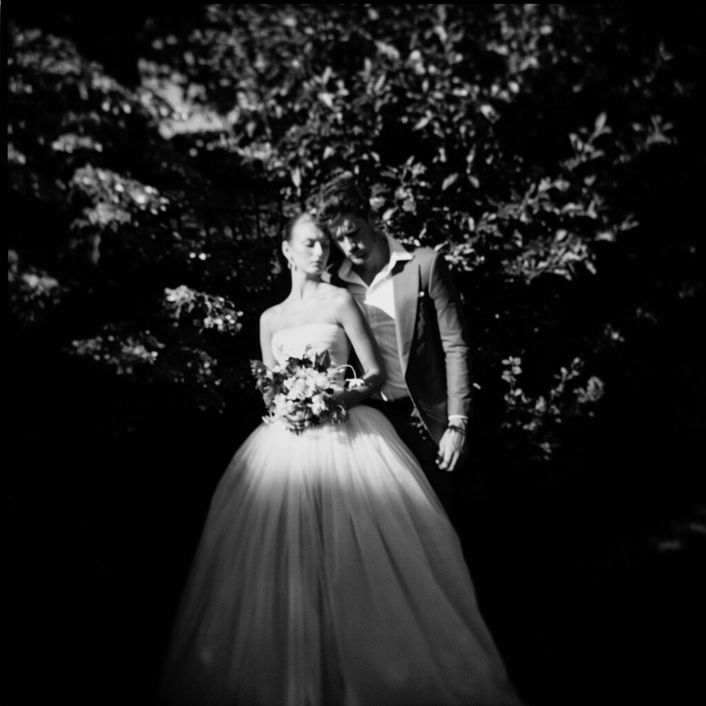 A bride and groom stand in dramatic light and shadow, their figures softly blurred, creating a dreamlike, ethereal effect.