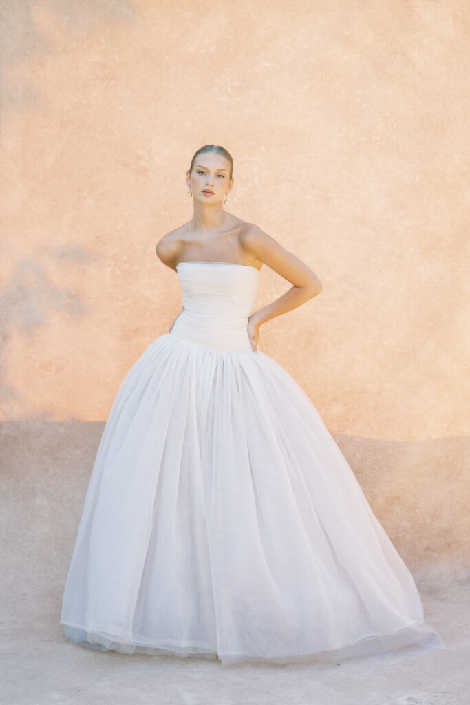 Elegant bride in a strapless white gown posing against a sunlit, textured wall at Greencrest Manor, captured by Lexie Vaccaro Photography.