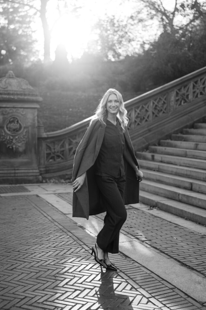 Black and white film-style portrait of a woman walking at Bethesda Terrace in Central Park, photographed by Lexie Vaccaro Photography during a fall engagement session.