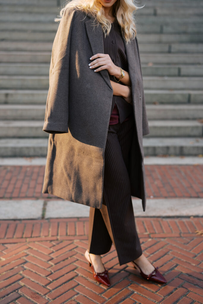 Detail shot of a woman’s fall outfit during a Central Park engagement session, photographed by Lexie Vaccaro Photography, featuring a tailored coat, pinstripe pants, and burgundy heels.
