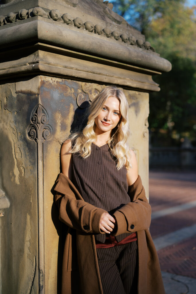 Portrait of a blonde woman in chic fall fashion leaning against Bethesda Terrace architecture in Central Park, photographed by Lexie Vaccaro Photography.