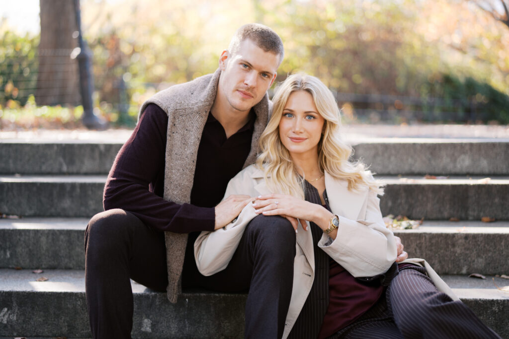 Fall engagement session in Central Park photographed by Lexie Vaccaro Photography, featuring a fashionable couple sitting together on stone steps in tailored autumn outfits.