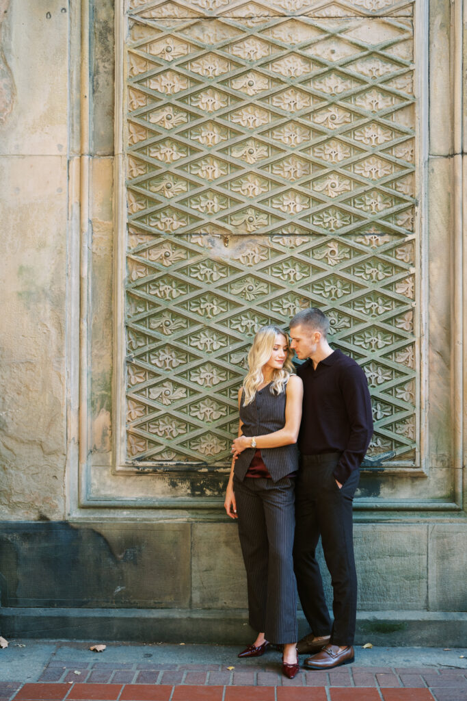 Central Park engagement session by Lexie Vaccaro Photography, featuring a fashionable couple standing against the ornate patterned wall at Bethesda Terrace.