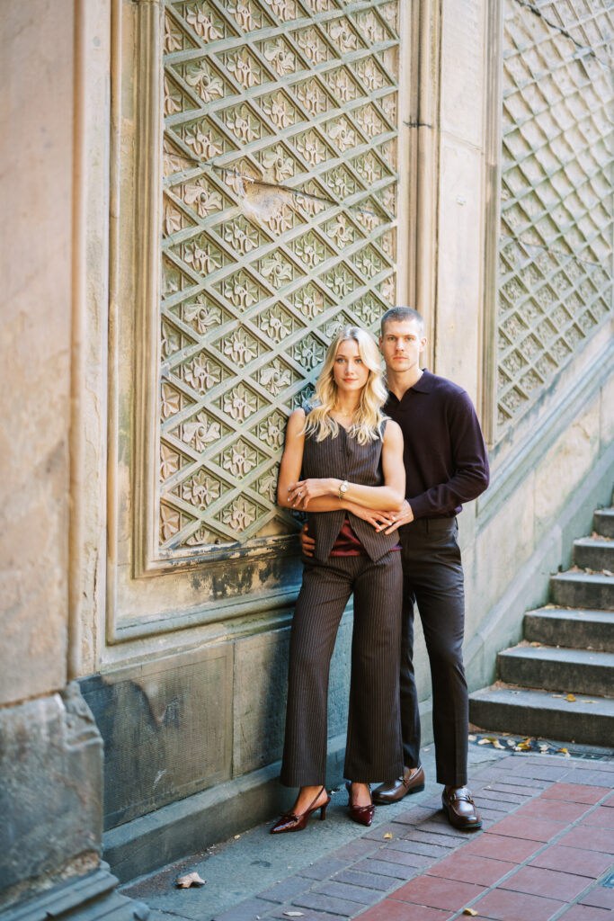 Fashion-forward couple leaning against the ornate patterned wall at Bethesda Terrace during a Central Park engagement session, photographed by Lexie Vaccaro Photography.