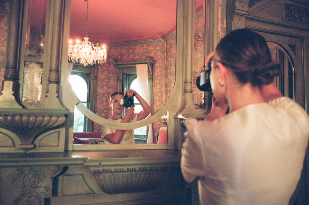 Film wedding photographer Lexie Vaccaro capturing self-portrait in antique mirror with vintage décor and chandelier