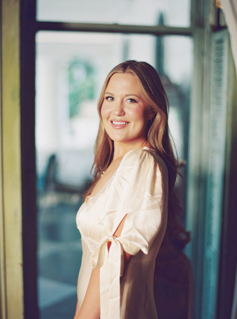Lexie Vaccaro smiling in soft light, wearing a silk dress with bow sleeves inside a historic venue