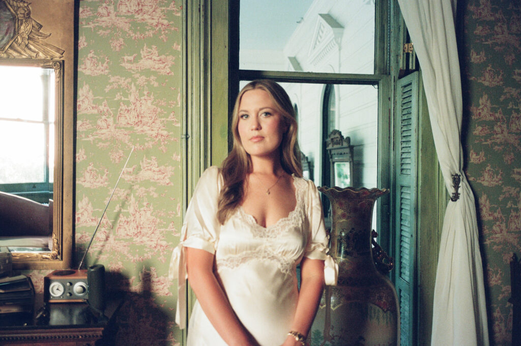 Lexie Vaccaro standing in a vintage room with toile wallpaper at The Columns Hotel in New Orleans wearing a silk Reformation dress