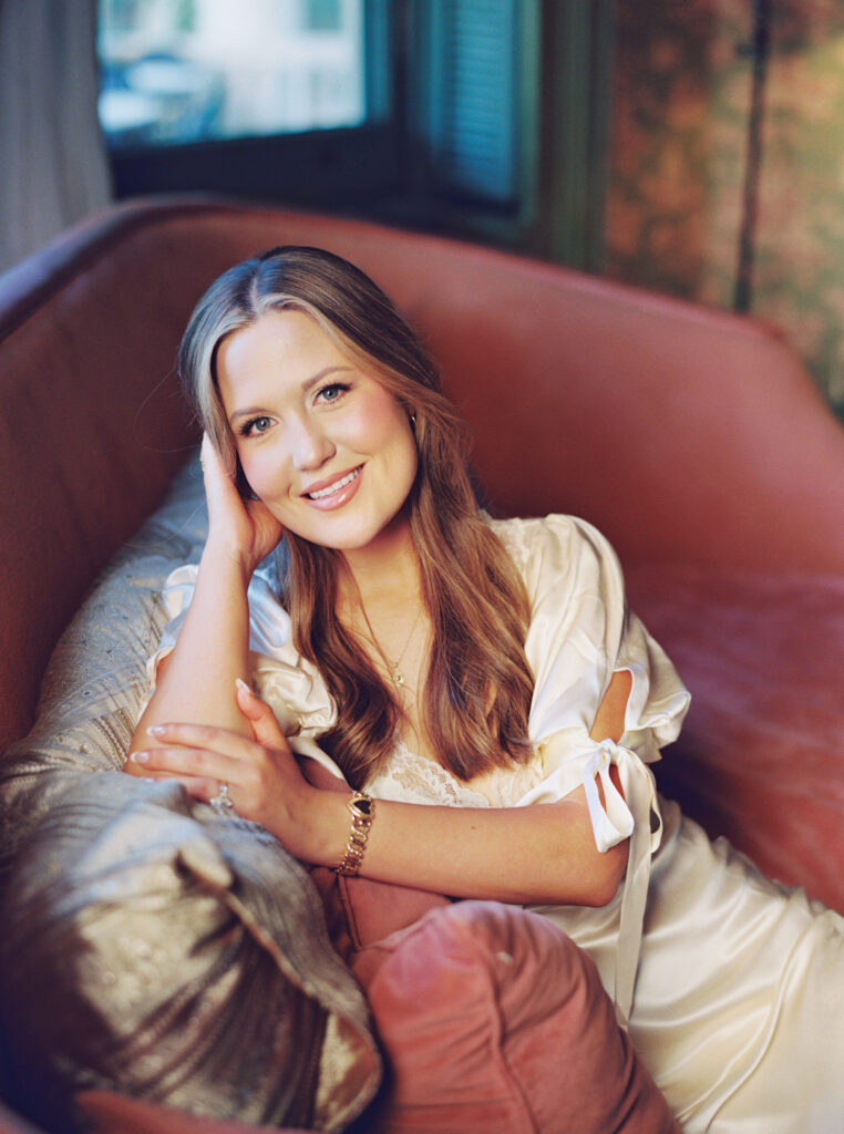 Lexie Vaccaro sitting on a velvet sofa at The Columns Hotel in a vintage silk Reformation dress, smiling warmly