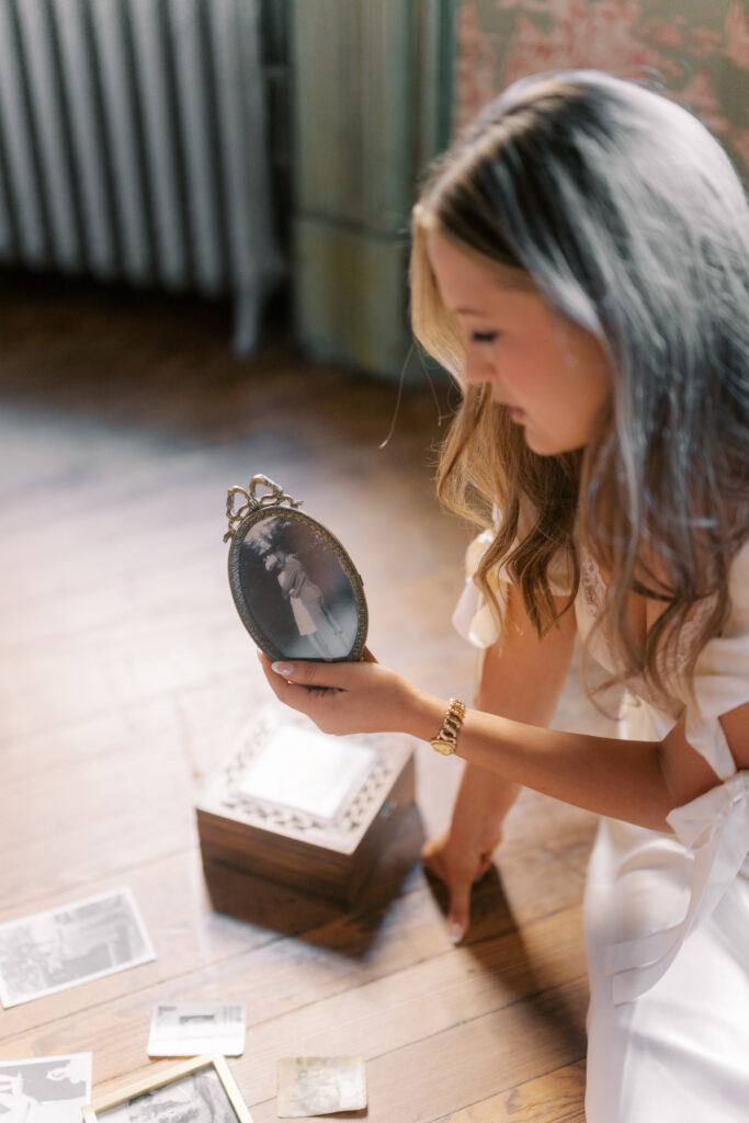 Lexie Vaccaro looking at a vintage family portrait while sitting on hardwood floor surrounded by heirloom photos