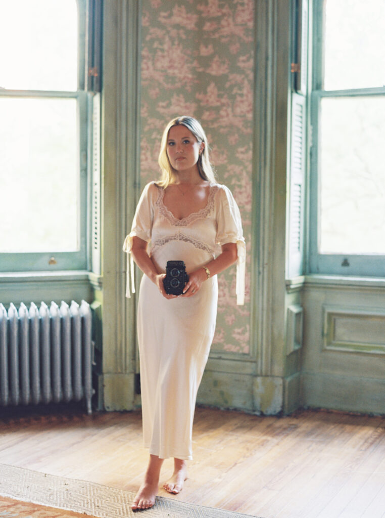 Fine art wedding photographer Lexie Vaccaro holding a vintage film camera in historic Southern interior