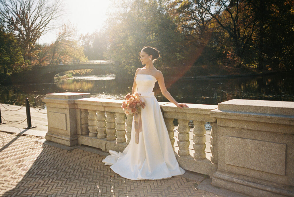 Bride holding bouquet and standing by the water at Prospect Park Boathouse during golden hour.