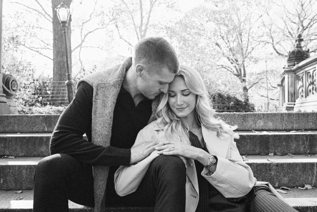 Black and white film photograph of a stylish couple sitting on the Bethesda Terrace steps in Central Park, captured by Lexie Vaccaro Photography during a fall engagement session.