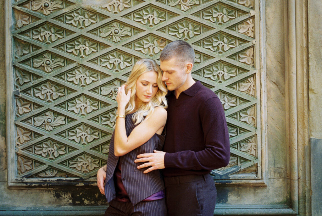 Central Park engagement session by Lexie Vaccaro Photography, featuring a fashionable couple in fall attire standing against the ornate patterned wall at Bethesda Terrace.
