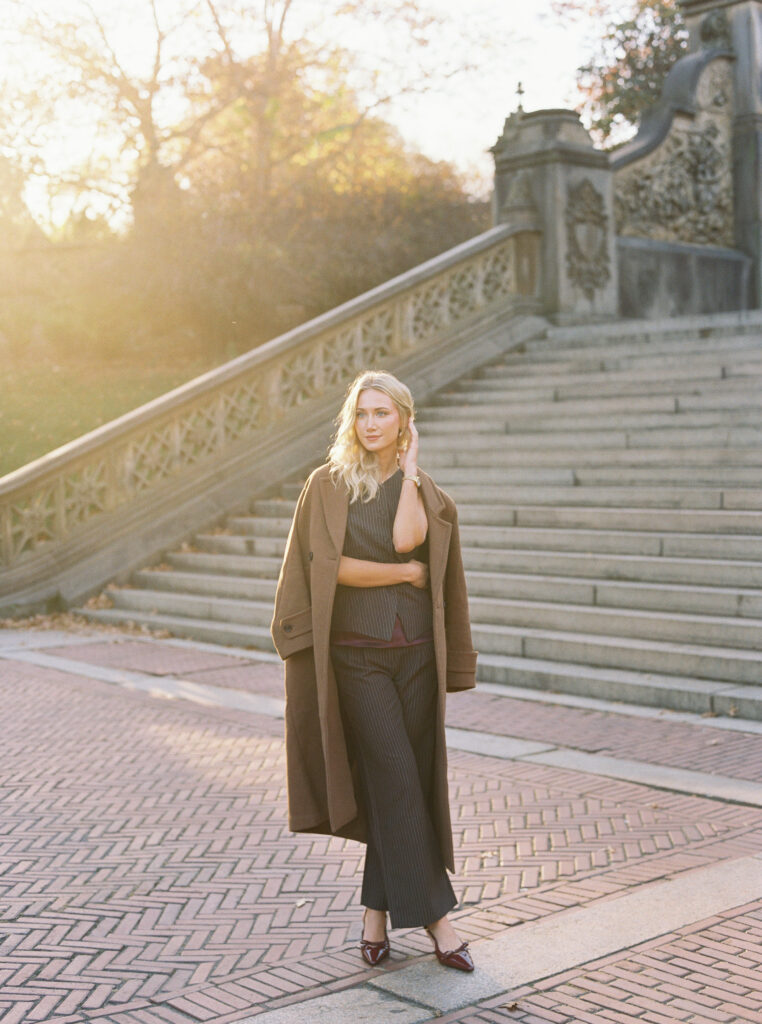 Full-length portrait of a blonde woman in tailored fall fashion walking near the Bethesda Terrace steps in Central Park, photographed on film by Lexie Vaccaro Photography.
