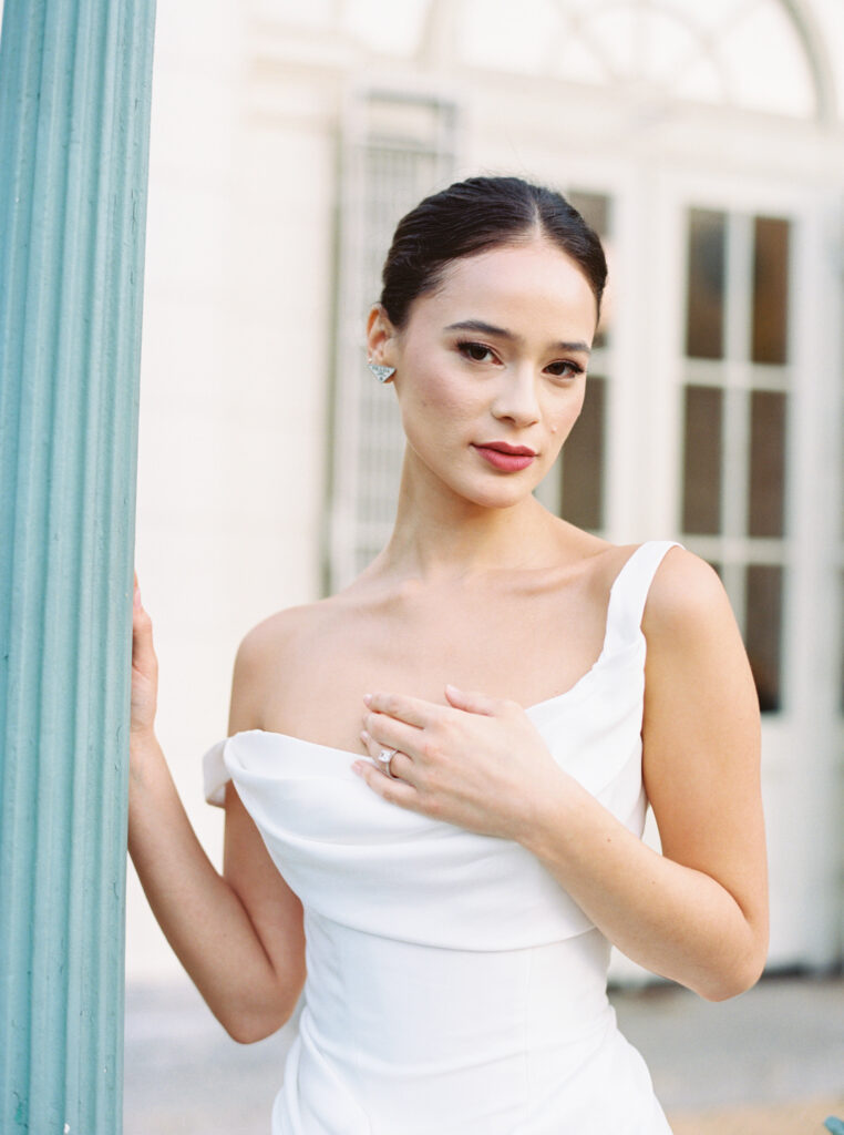 Bride in draped white Renhue gown posing with hand on chest outside Purslane at the Boathouse, photographed on film by Lexie Vaccaro Photography