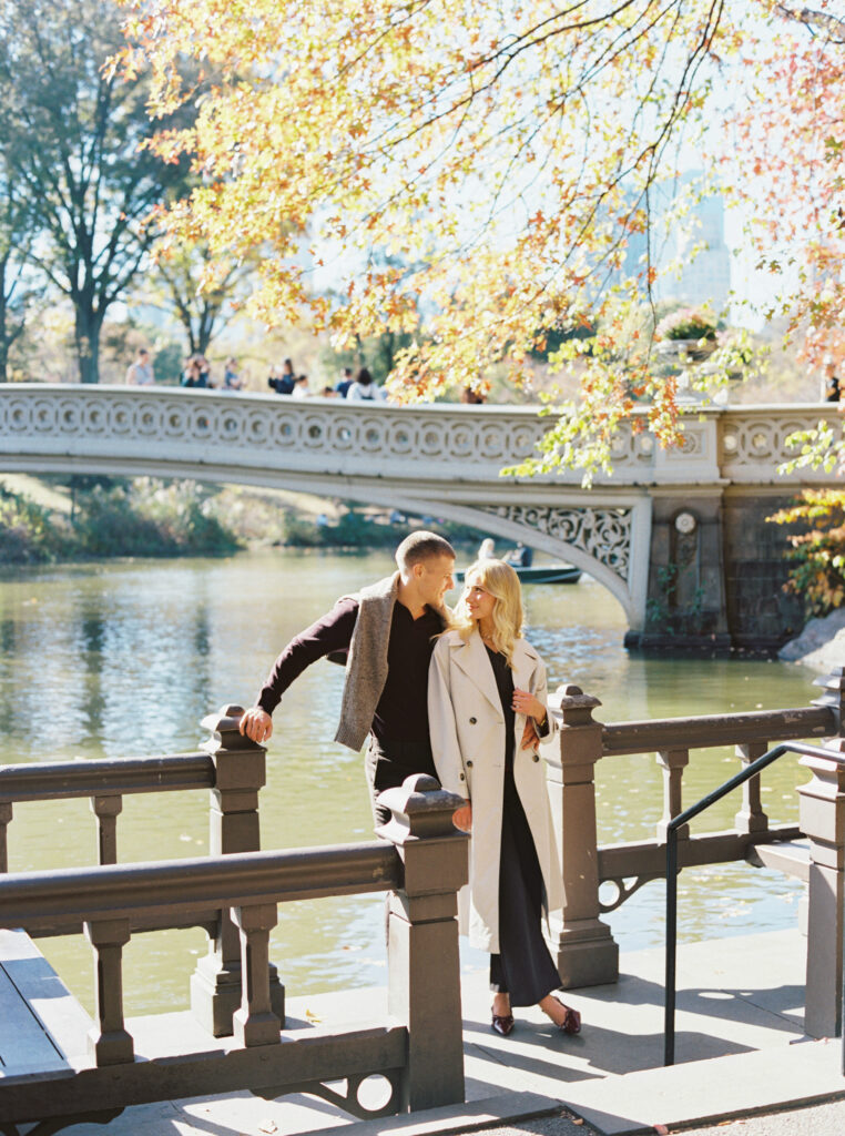 Fall Central Park engagement session by Lexie Vaccaro Photography, featuring a stylish couple standing near Bow Bridge under golden autumn leaves.