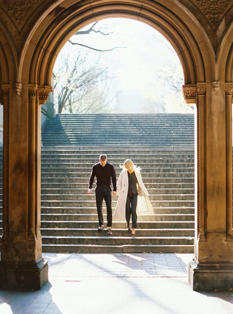 Film photograph of a couple walking down the Bethesda Terrace steps in Central Park, framed by the grand arches, captured by Lexie Vaccaro Photography during a fall engagement session.