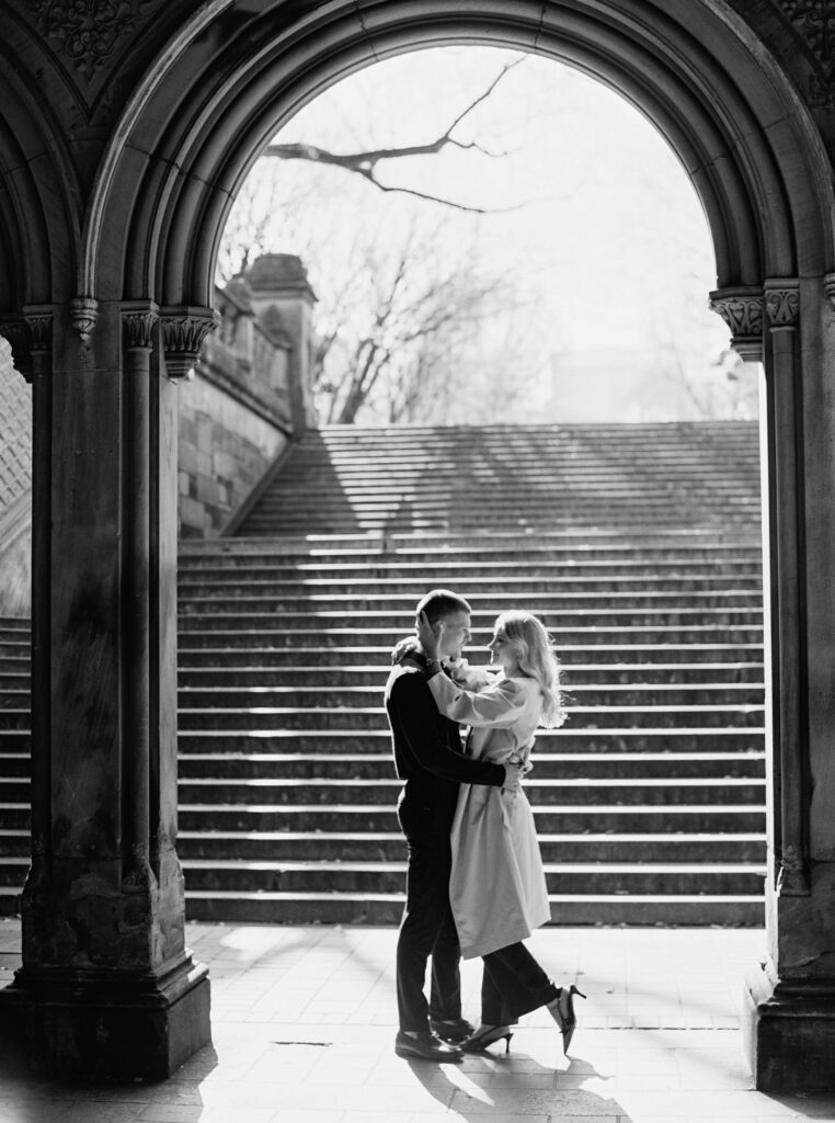 Black and white film photograph by Lexie Vaccaro Photography of a stylish couple framed by the arches at Bethesda Terrace in Central Park, New York City.