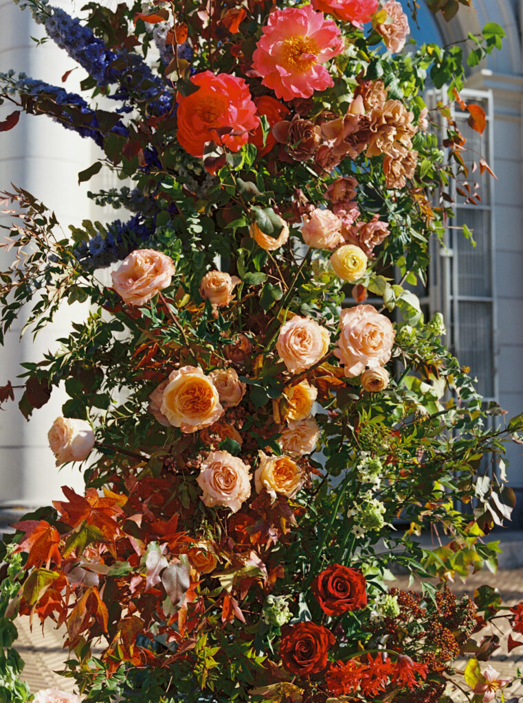 Colorful wedding flower installation with garden roses, red leaves, and vibrant blooms in fall tones