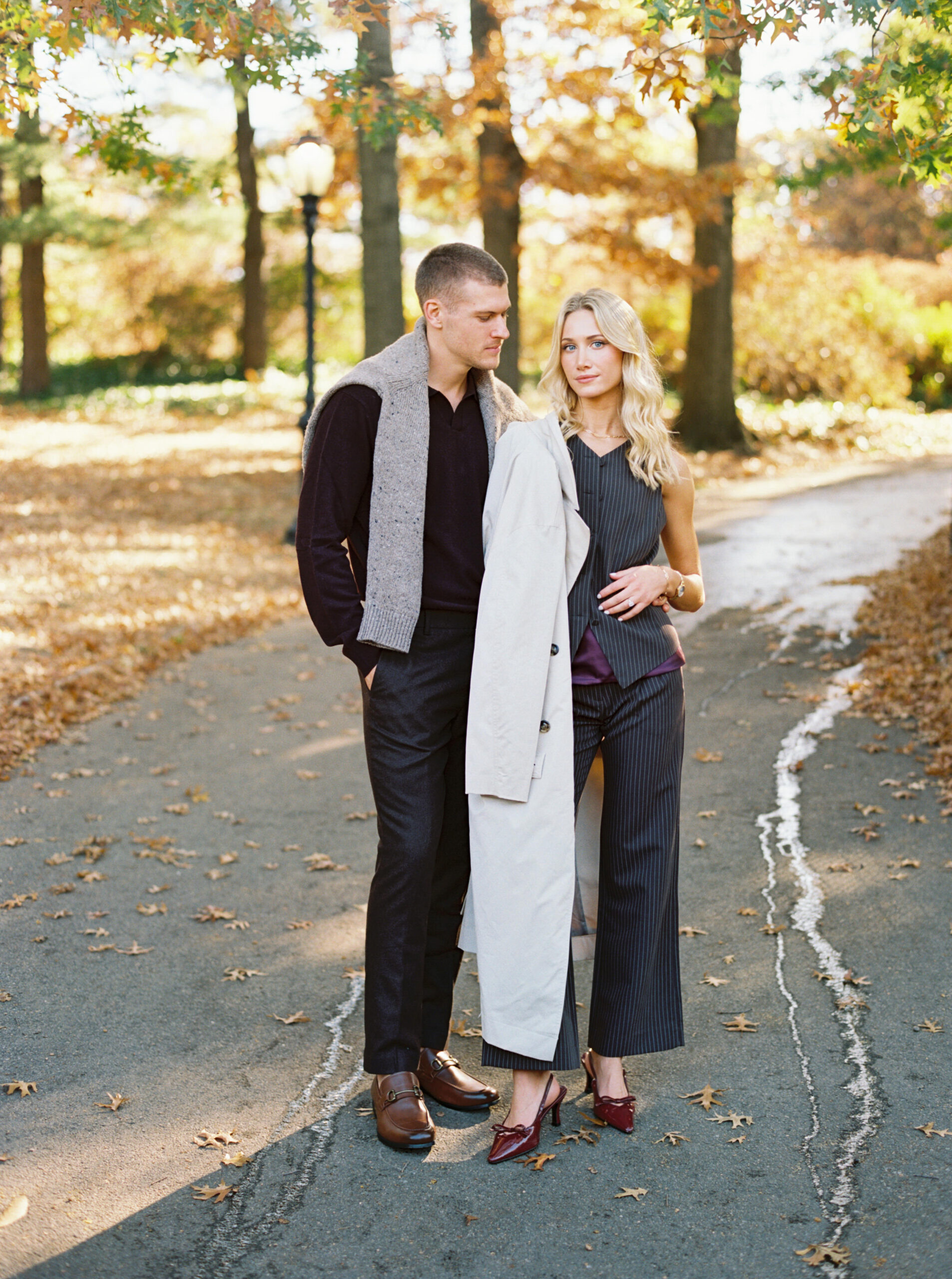 Fall Central Park engagement session photographed on film by Lexie Vaccaro Photography, featuring a stylish couple in tailored fall outfits standing on a tree-lined path.