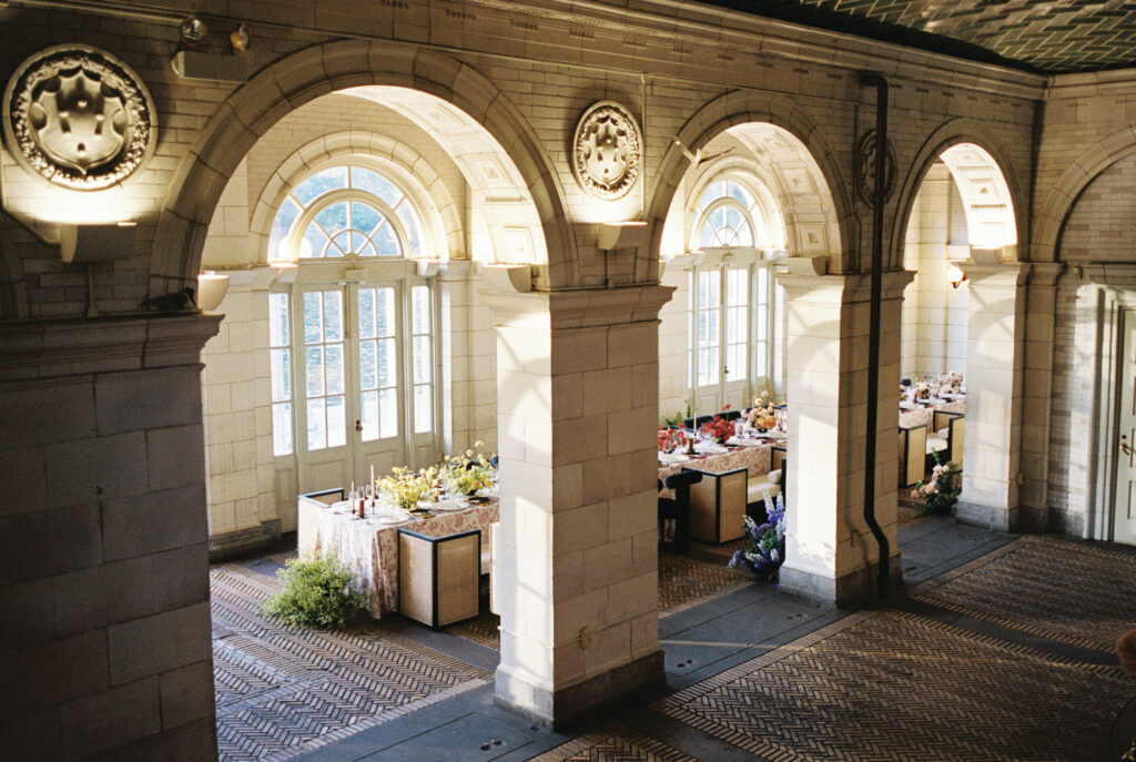 Indoor wedding reception setup with floral linens, modern chairs, and arched windows at Prospect Park Boathouse.