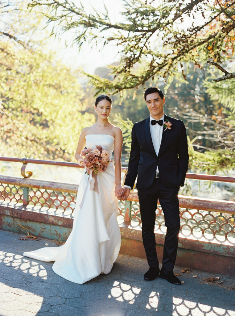 Bride and groom holding hands in front of an ornate railing at Prospect Park Boathouse in Brooklyn, captured on film by Lexie Vaccaro Photography.