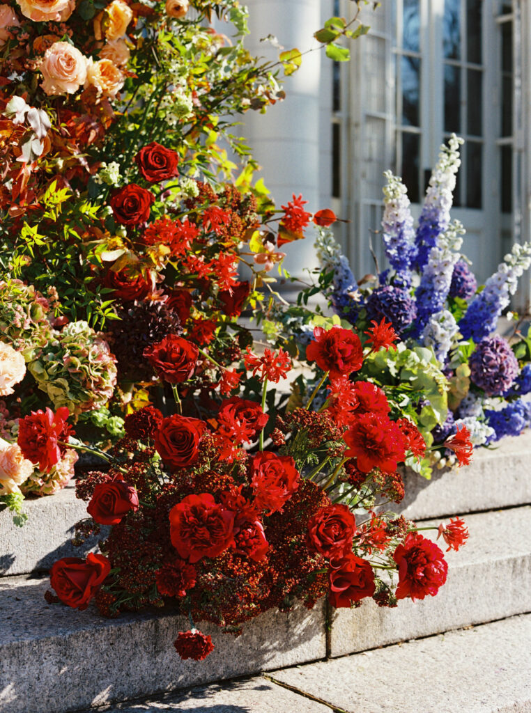 Close-up of red roses and purple delphiniums on the stone steps of Purslane at the Boathouse, captured on film by Lexie Vaccaro Photography