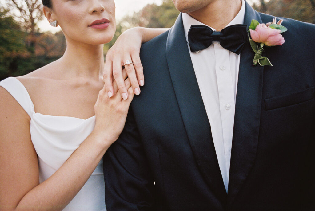 Close-up of a bride's hand resting on the groom's arm, showing her engagement ring, with the couple dressed in formal wedding attire
