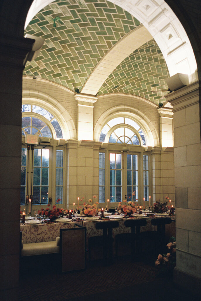 Candlelit wedding reception setup in historic arched room with green tiled ceiling, floral tablescape, and floor-to-ceiling windows
